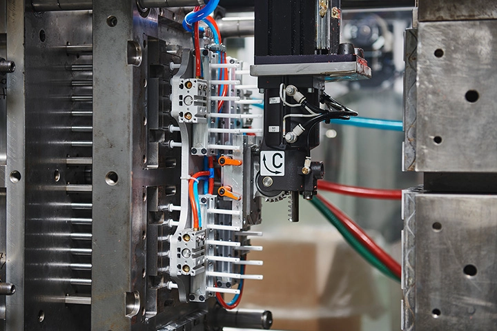 The plungers of the oral dosing syringes have just been injected and the mould is open. The robot is removing the plungers from their cavities.