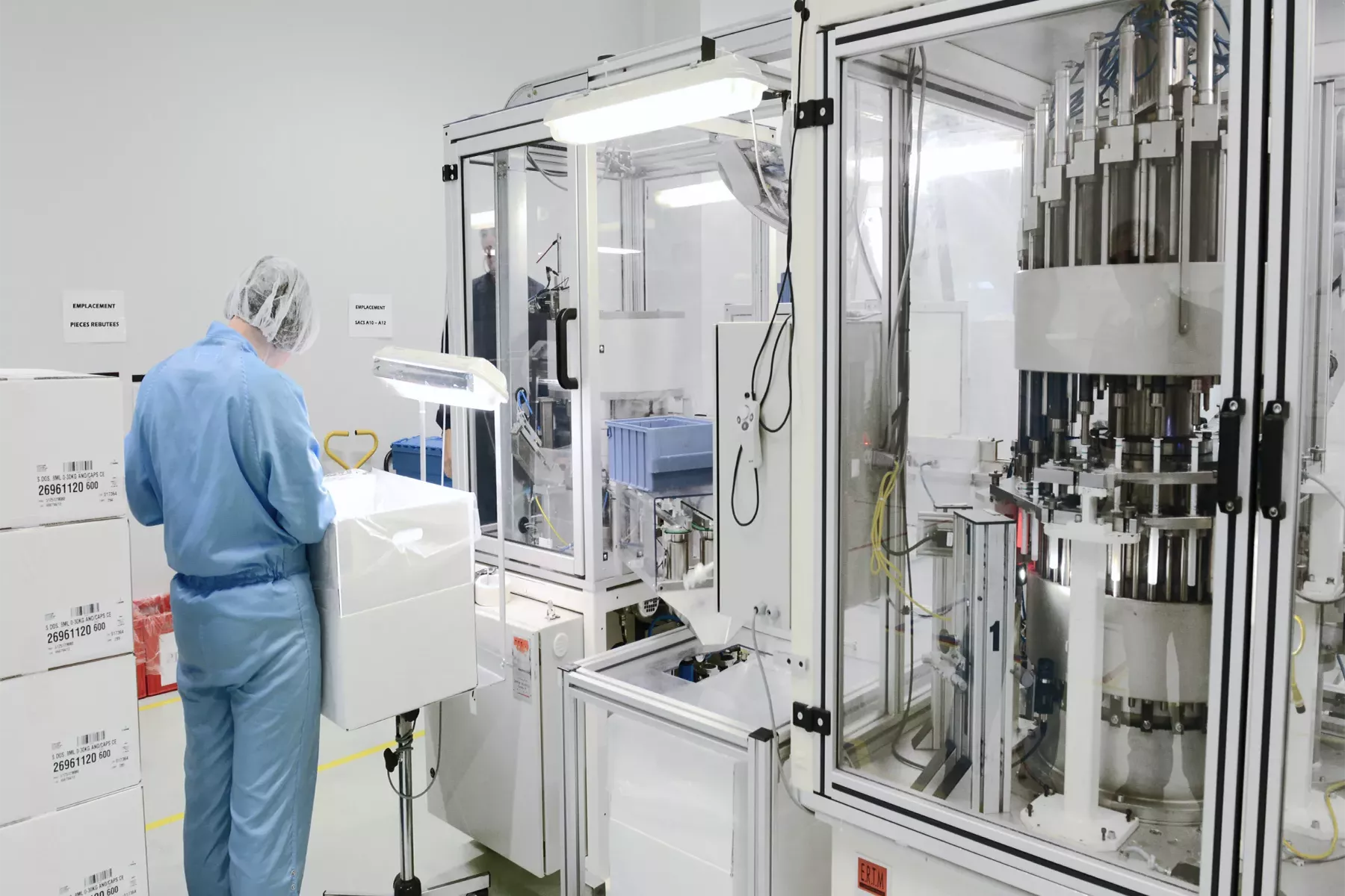 Technicien effectuant un contrôle qualité à côté d'une machine assemblant des pistons avec des corps de pipettes doseuses