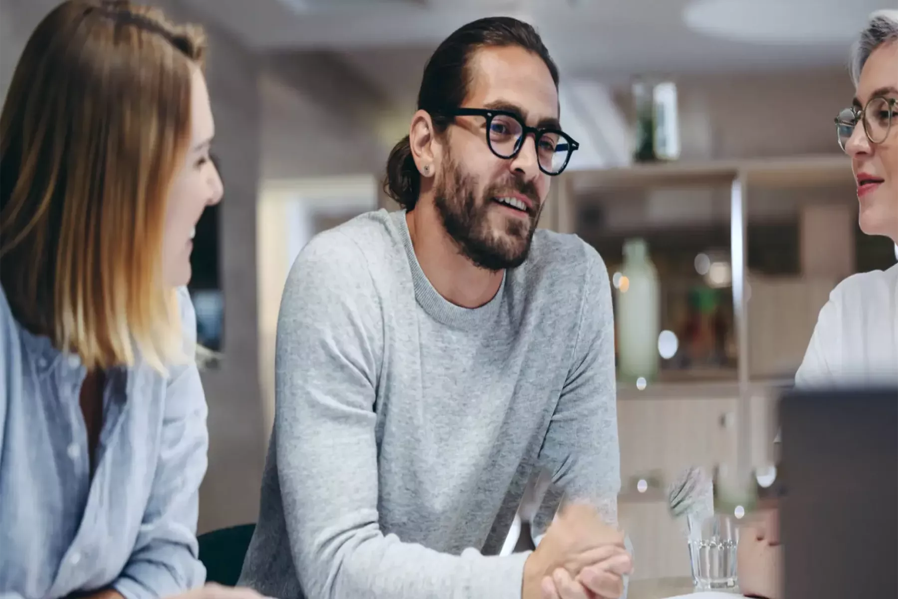 Deux femmes et un homme assis à une table et discutant